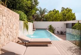 Teresa Gestora de alquiler. Piscina moderna con tumbonas y pared de piedra, rodeada de vegetación tropical, ideal para un alojamiento de lujo o villa.