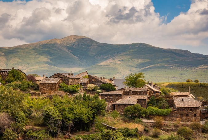 Teresa gestora de alquiler vacacional. Vista de un pueblo rural en las montañas con casas de piedra y vegetación. View of a rural village in the mountains with stone houses and vegetation.